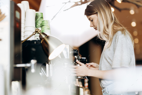 A good looking slim blonde with long hair,dressed in casual outfit,is cooking coffee in a modern - Stock Photo - Images