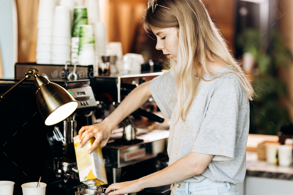 A good looking slim blonde with long hair,dressed in casual outfit,is cooking coffee in a modern - Stock Photo - Images