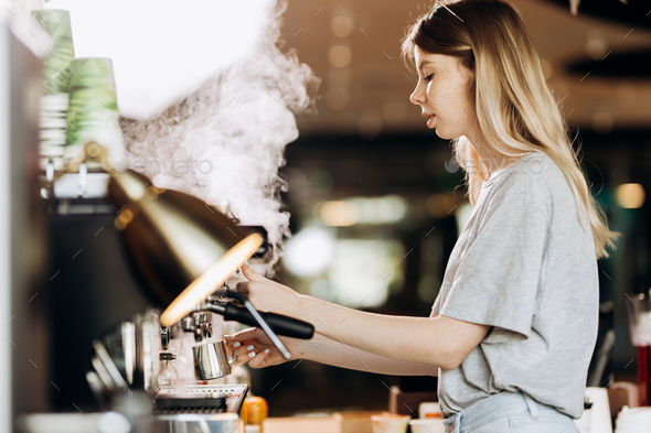A good looking slim blonde with long hair,dressed in casual outfit,is cooking coffee in a modern - Stock Photo - Images
