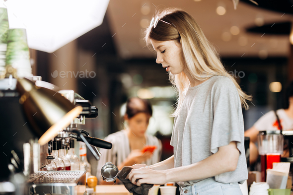 A good looking slim blonde with long hair,dressed in casual outfit,is cooking coffee in a modern - Stock Photo - Images