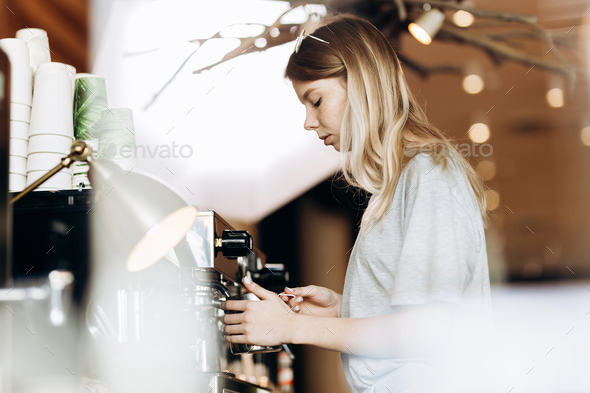 A good looking slim blonde with long hair,dressed in casual outfit,is cooking coffee in a modern - Stock Photo - Images