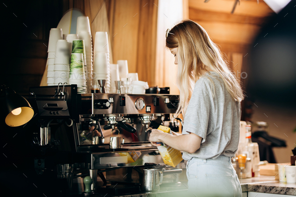 A good looking slim blonde with long hair,dressed in casual outfit,is cooking coffee in a modern - Stock Photo - Images