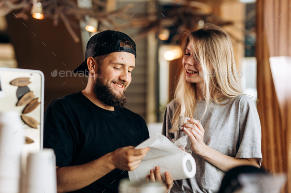 Two young smiling people,a blonde girl and man with beard.dressed in casual outfit, stand next to - Stock Photo - Images