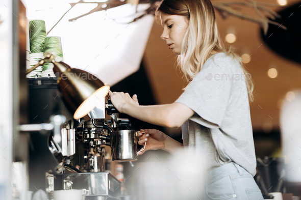 A good looking slim blonde with long hair,dressed in casual outfit,is cooking coffee in a modern - Stock Photo - Images