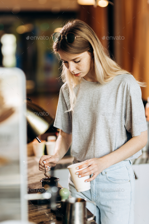 A good looking slim blonde with long hair,dressed in casual outfit,is cooking coffee in a modern - Stock Photo - Images