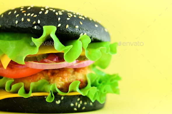Macro view of tasty black burger with beef, cheese, lettuce, onion, tomatoes on yellow background - Stock Photo - Images