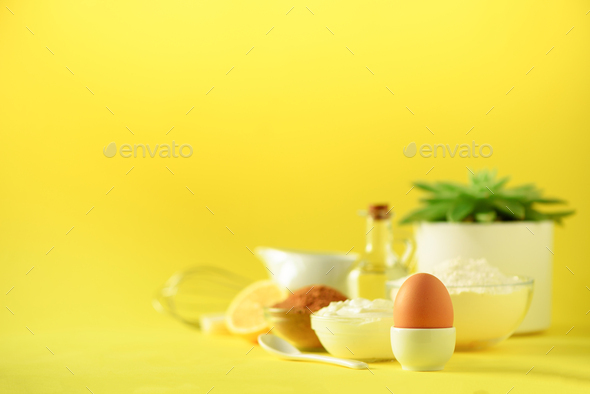 Healthy baking ingredients - butter, sugar, flour, eggs, oil, spoon, brush, whisk, milk over yellow - Stock Photo - Images