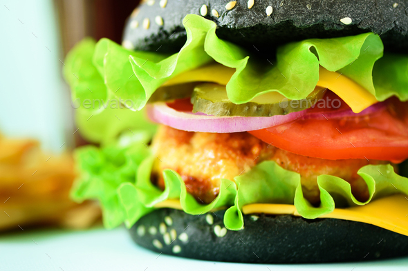 Macro view of tasty black burger with beef, cheese, lettuce, onion, tomatoes on blue background - Stock Photo - Images
