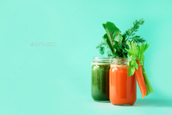 Two bottles of green and orange smoothies on blue background. Detox drinks in glass jar from - Stock Photo - Images