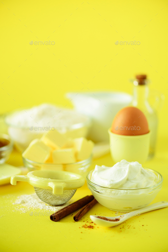 Healthy baking ingredients - butter, sugar, flour, eggs, oil, spoon, rolling pin milk over yellow - Stock Photo - Images