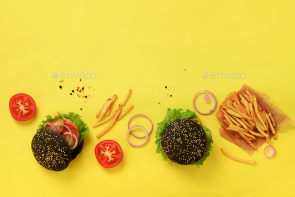 Black burgers with beef, tomato, cheese, onion, cucumber and lettuce on yellow background. Top view - Stock Photo - Images