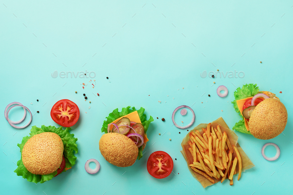 Tasty burgers with beef, tomato, cheese, onion, cucumber and lettuce on blue background. Top view - Stock Photo - Images