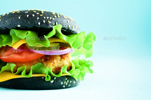 Macro view of tasty black burger with beef, cheese, lettuce, onion, tomatoes on blue background - Stock Photo - Images