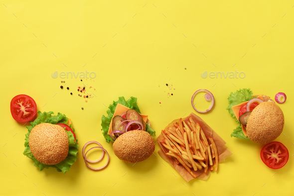 Tasty burgers with beef, tomato, cheese, onion, cucumber and lettuce on yellow background. Top view - Stock Photo - Images
