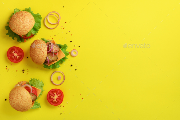 Delicious burgers, cheese, lettuce, onion, tomatoes on yellow background. Close up banner. Unhealthy - Stock Photo - Images