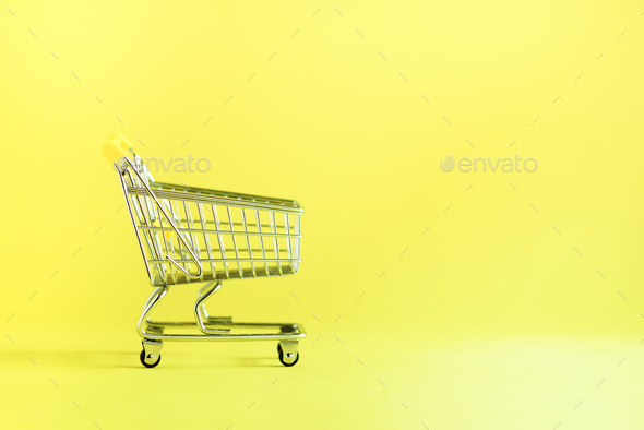 Shopping cart on yellow background. Minimalism style. Creative design. Copy space. Shop trolley at