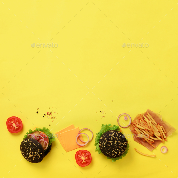 Black burger, french fries potatoes, tomatoes, cheese, onion, cucumber and lettuce on yellow - Stock Photo - Images