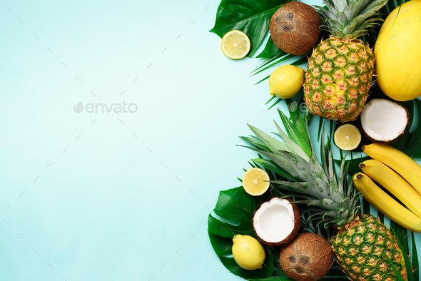 Exotic pineapples, ripe coconuts, banana, melon, lemon, tropical palm and green monstera leaves on - Stock Photo - Images
