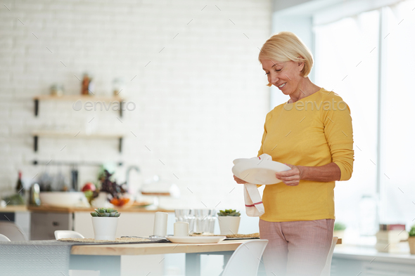 Mature woman wiping plate with dish towel - Stock Photo - Images