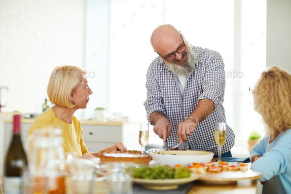 Content mature man cutting meat for guests - Stock Photo - Images