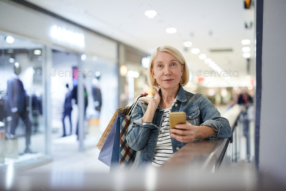 Attractive mature lady sending photo message to friend during shopping - Stock Photo - Images