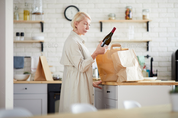 Mature lady unpacking paper bags in kitchen - Stock Photo - Images