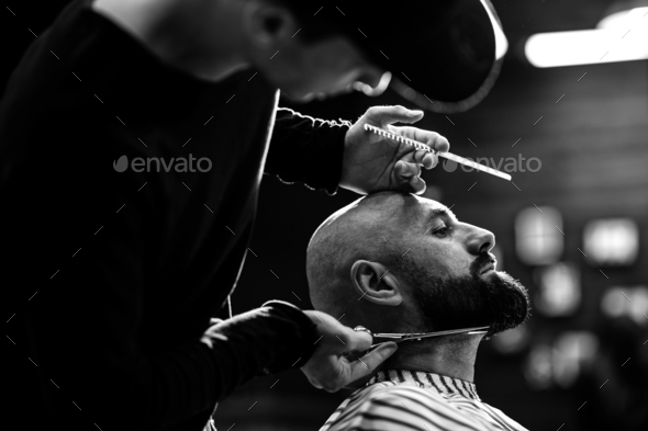 Black and white photo. Fashion barber dressed in a black clothes tidies up men's beard  and - Stock Photo - Images