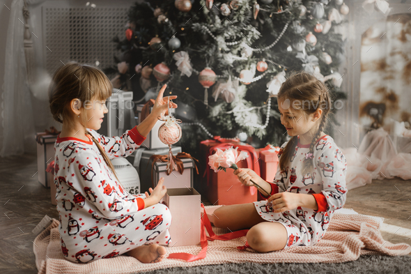 Two little sisters in pajamas sit on the carpet and open New Yea - Stock Photo - Images