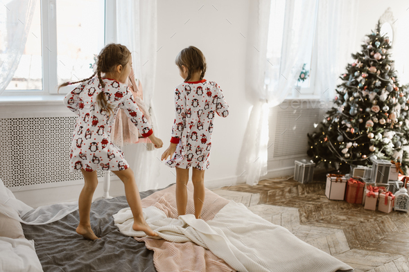 Two charming little girls in their pajamas are having fun jumping on a bed in a sunlit cozy bedroom - Stock Photo - Images