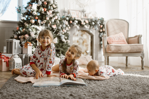 Two little sisters and a tiny brother lie on the carpet and read - Stock Photo - Images