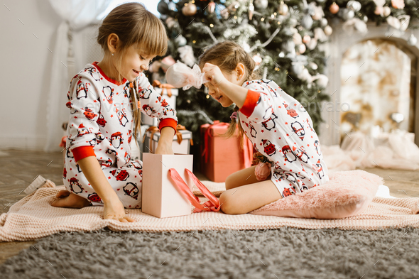 Two little sisters in pajamas sit on the carpet and open New Yea - Stock Photo - Images