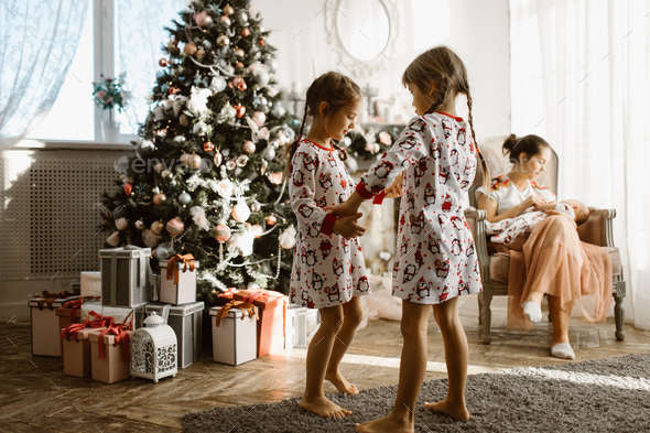 Two little sisters in pajamas having fun New Year's tree with gi - Stock Photo - Images