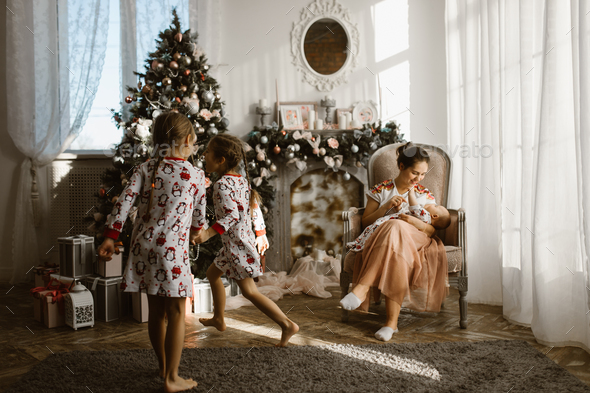 Two little sisters in pajamas having fun New Year's tree with gifts in the light cozy room and - Stock Photo - Images