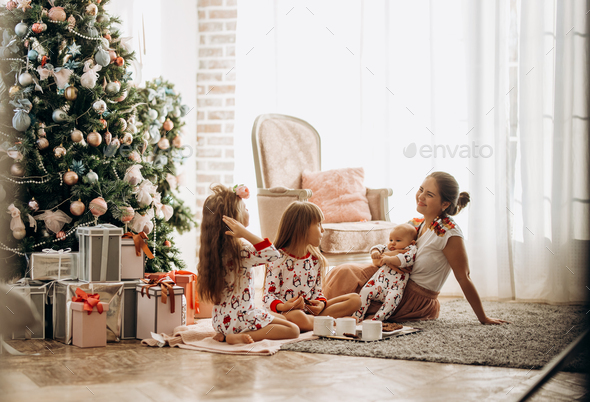 Mother with a baby on her hands sits o the carpet with her two daughters dressed in pajamas eating - Stock Photo - Images