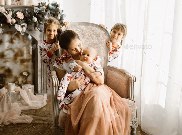 Beautiful mother sits with her little baby in the armchair next to the fireplace in the light cozy - Stock Photo - Images