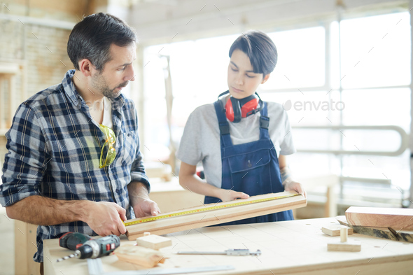Carpenters checking measurement of wooden plank - Stock Photo - Images