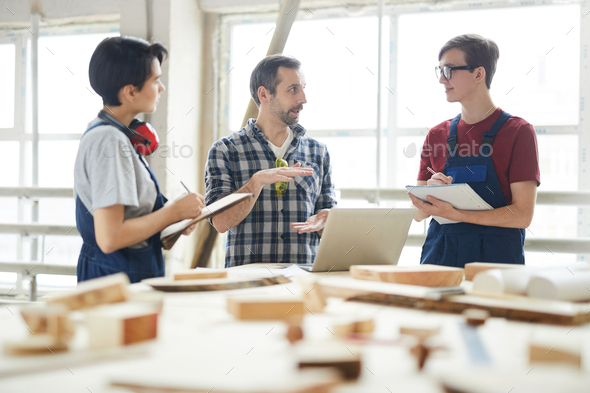 Chief carpenter giving class for interns in workshop - Stock Photo - Images