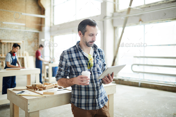 Busy young joiner reading article on tablet - Stock Photo - Images