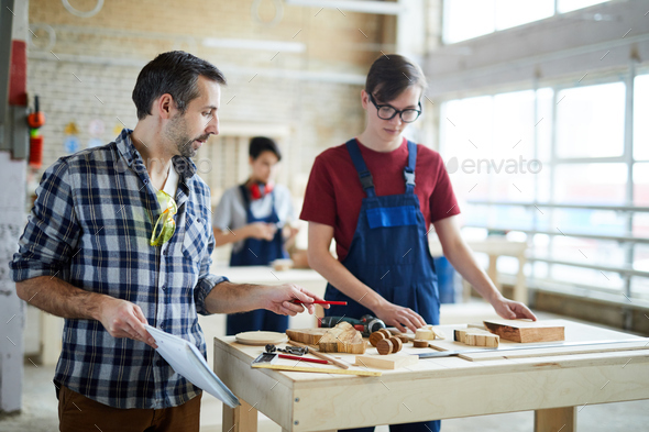 Carpenter giving advice to student in workshop - Stock Photo - Images
