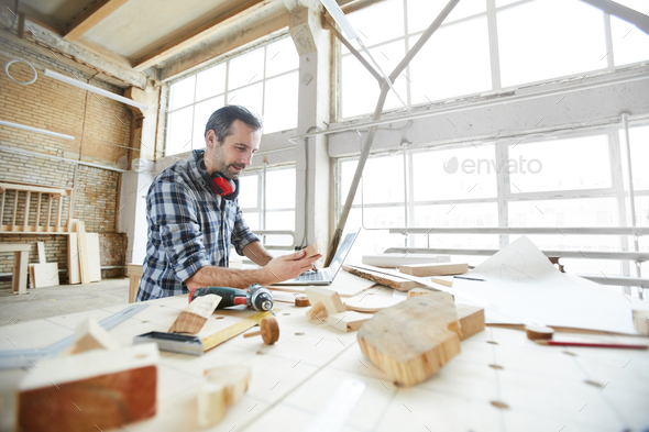 Carpenter searching for information on Internet while checking wooden details - Stock Photo - Images