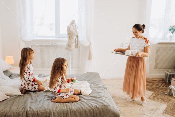 Young beautiful mother is bringing cocoa with Marshmallows and cookies to her daughters sitting on - Stock Photo - Images