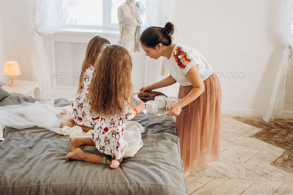 Young beautiful mother is bringing cocoa with Marshmallows and cookies to her daughters sitting on - Stock Photo - Images