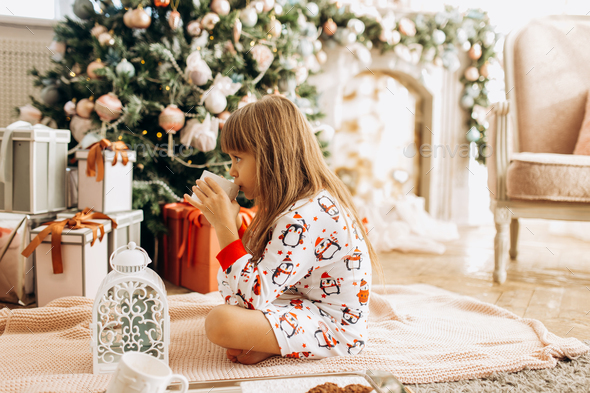 Little girl dressed in pajama sits o the carpet and drinks a co - Stock Photo - Images