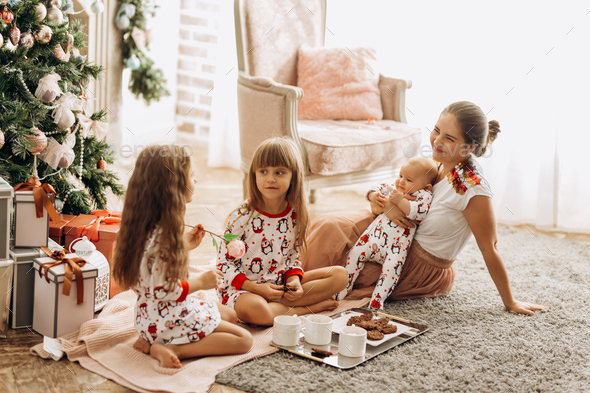 Mother with a baby on her hands sits o the carpet with her two daughters dressed in pajamas eating - Stock Photo - Images