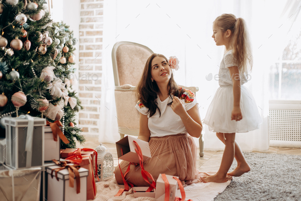 Happy young mother with flower in her hair and her little daughter in nice dress sit near the New - Stock Photo - Images