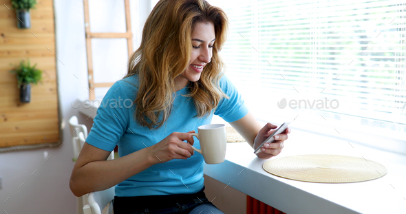 Beautiful blond woman drinking coffee and reading news - Stock Photo - Images