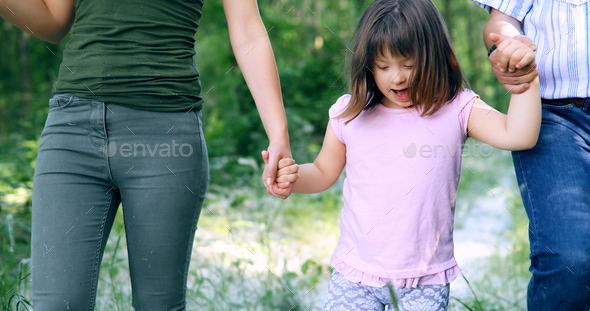 Beautiful little girl with down syndrome walking with parents - Stock Photo - Images