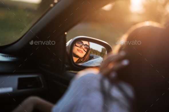 Reflection of a beautiful young dark-haired girl in sunglasses in a side mirror of a car - Stock Photo - Images