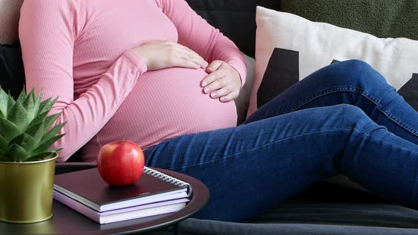 Pregnant woman touching her belly while sitting on the couch