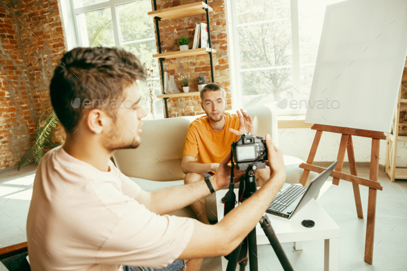Two young male bloggers with professional camera recording video interview at home